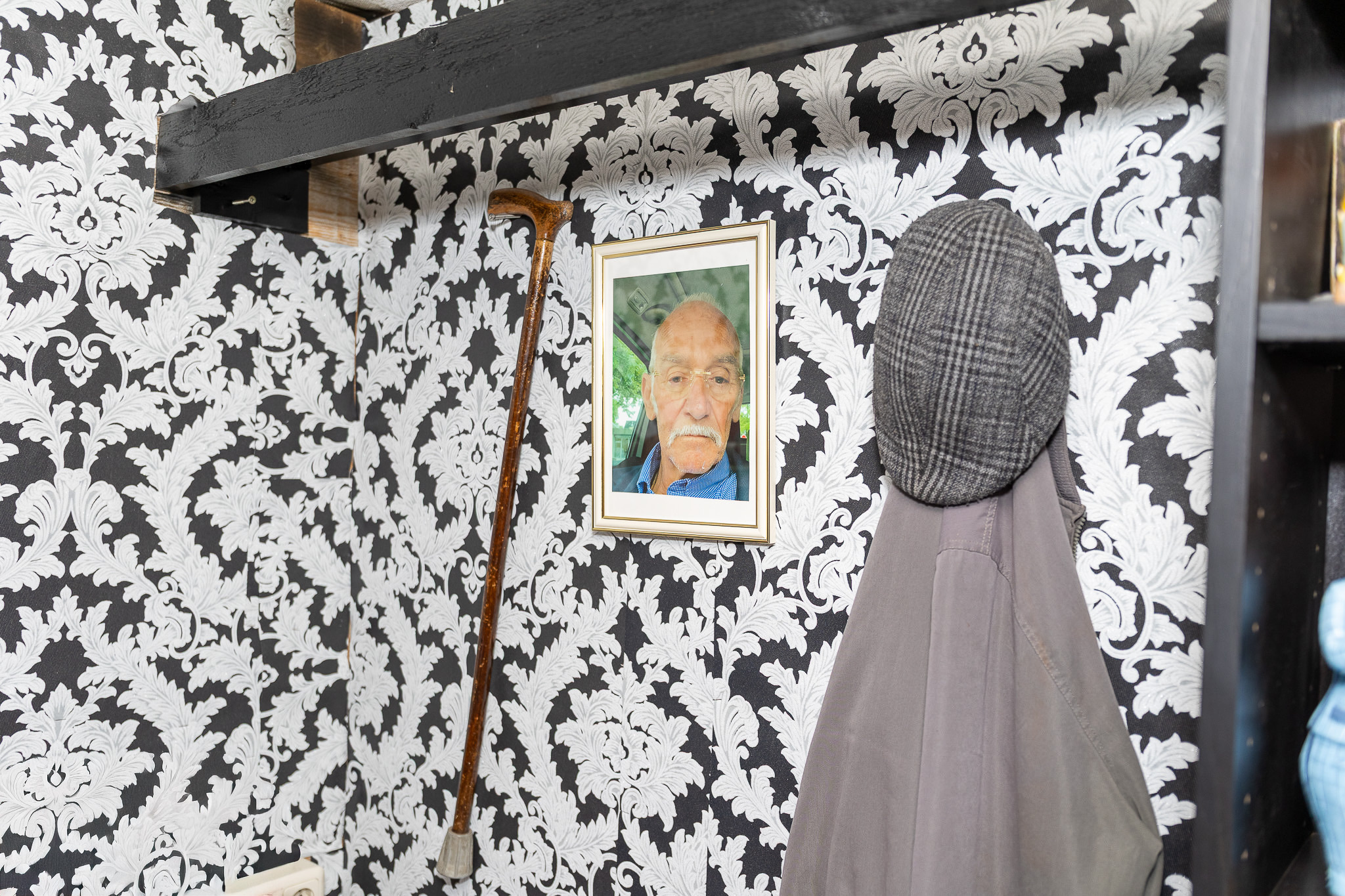 Ingelijst portret van opa De Vries aan de muur van de werkplaats, naast zijn pet en wandelstok